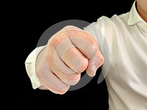 A man holds a fist in front of him. A man in a white shirt shows a hand gesture, on a black background. Concept: aggression, anger