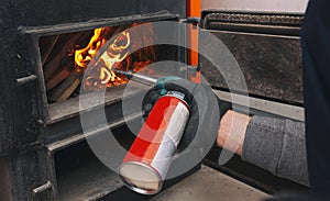 A man holds a gas burner and makes a fire in the solid fuel boiler in the boiler room.