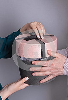 Man holds a gift and girl opens it.Round box with gift in hands of couple
