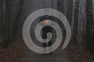 Man holds Halloween pumpkin in dark autumn forest