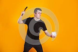 Man holds a hammer that is raised above a piggy bank with money to break it.