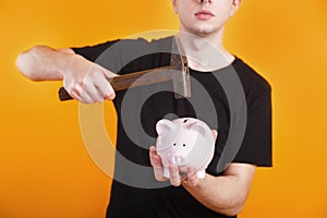 Man holds a hammer that is raised above a piggy bank with money to break it.