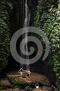 A man holds the hand of a beautiful woman at a waterfall. A couple in love on a waterfall. Honeymoon trip. Happy couple