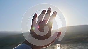 Man holds hand trying to hide bright sun in clear blue sky