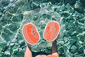 Man holds in hands two melon halfs and stands in crystal clear s