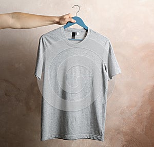 Man holds a hanger with blank gray t-shirt on brown background