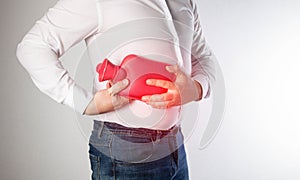 The man holds a heating pad with hot water on the abdominal wall on the right. Relieve muscle spasms and pain near diseased photo