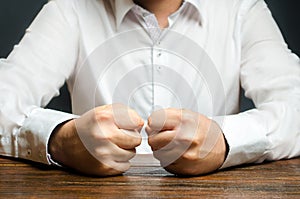 A man holds his closed fists on the table. The end of patience. It is impossible to bear it. An attack of anger, stress. photo