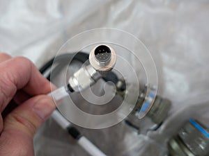 A man holds in his hand a round eight-pin metal cable connector.