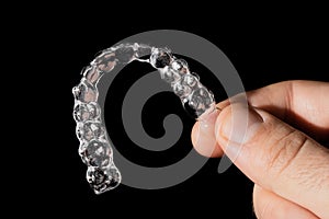 A man holds in his hand transparent aligners plastic braces retainers for straightening teeth on a black background