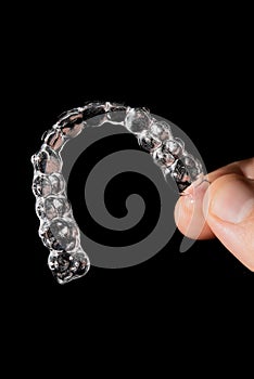 A man holds in his hand transparent aligners plastic braces retainers for straightening teeth on a black background