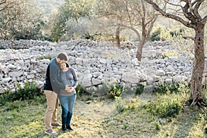 Man holds his hands on the belly of a pregnant woman in the park against the background of stones