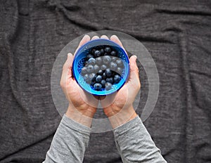 A man holds in his hands fresh blueberries in a bowl on black background