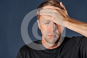 A man holds his hands on his head on blue background. Headache and cold.