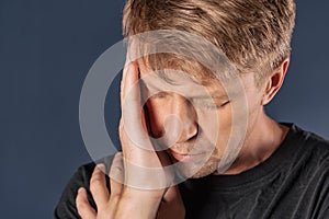 A man holds his hands on his head on blue background. Headache or migraine.