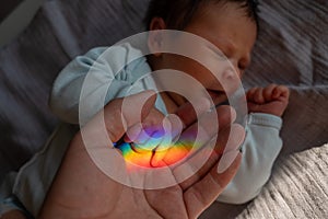 A man holds his newborn son's hand. Beam of light through a prism.
