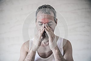 The man holds his nose and sinus area with fingers in obvious pabvious pain from a head ache in the front forehead area.