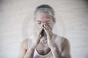 The man holds his nose and sinus area with fingers in obvious pain from a head ache in the front forehead area