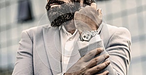 Man holds his watch. Portrait successful businessman in a business suit, using the watch on a city background