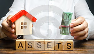 A man holds a house and a bundle roll of Euro over the word Assets. Declaration income and taxation, audit of ownership