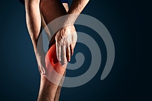 A man holds a leg that hurts, a man on a dark background, close-up, pain indicated in red. photo