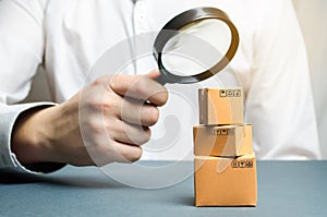 A man holds a magnifying glass above the boxes. Examination of goods for the presence of contraband, prohibited goods, defects.