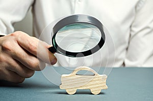 A man holds a magnifying glass over a miniature wooden car. The estimated cost of the auto. Analysis and technical inspection of