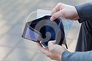 Man holds a medical mask and empty wallet without money. Bankruptcy and unemployment resulting from the global coronavirus photo