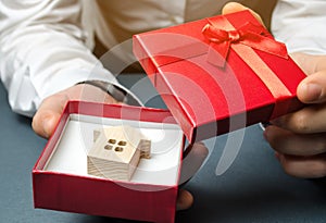 Man holds a miniature house in a gift box. Housing as a gift. Win an apartment in the lottery. To inherit property. Holiday