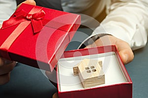 Man holds a miniature house in a gift box. Housing as a gift. Win an apartment in the lottery. To inherit property. Holiday photo