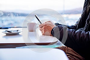 A man holds a mobile phone in his hand and writes a message, next to it is a cup of coffee