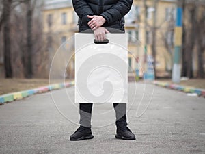 A man holds a mockup white plastic bag. A man with a package on the street in the park