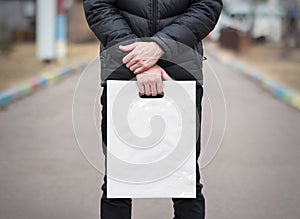 A man holds a mockup white plastic bag. A man with a package on the street in the park