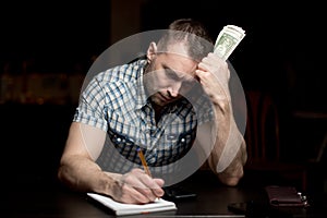 Man holds a modest amount of money and makes notes in a notebook