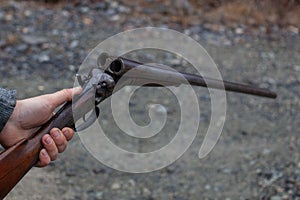 A man holds an old, antique, double-barrel break action shotgun out, ready to load two rounds into the bore.