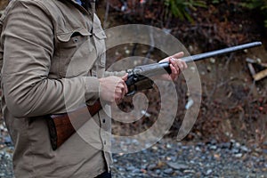 A man holds an old, antique, double-barrel shotgun to his waist, pointing the barrel downrange, ready to load