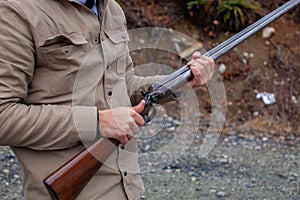A man holds an old, antique, double-barrel shotgun to his waist, pointing the barrel downrange, ready to load