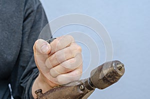 A man holds an old manual drill in his hand. A rusty metal hand