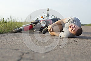 A man holds onto his knee, lying on the asphalt near the motorcycle, the theme of road accidents