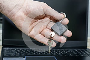 a man holds an open padlock with keys in his hand against the background of a laptop the concept of data protection