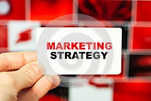 A man holds out a business card on a red background with the words - Marketing strategy