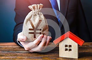 Man holds out a chinese yuan or japanese yen bag near the house. Home purchase, invest in real estate. Property appraisal.