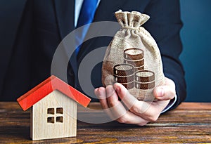 Man holds out a money bag near the house. Home purchase, invest in real estate. Property appraisal. Favorable terms and conditions