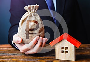 Man holds out a russian ruble bag near the house. Bank approval for issuing a mortgage loan. Property appraisal. Favorable terms