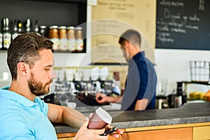 Man holds paper cup with coffee barista guy stand on background. Client got his drink. Drinks to go useful option in