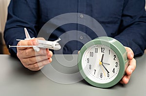 A man holds a passenger plane and a clock. Flight time. Planning a route with transfers