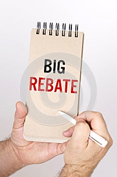 A man holds a pen and a bolknot in his hands with the inscription - Big Rebate