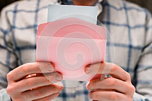 A man holds a pink envelope and reads a love letter