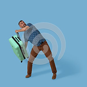 Man holds plastic suitcase posing in studio on blue background. Caucasian man going to throw his green suitcase with