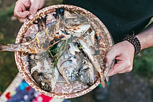 A man holds a plate with a ready meal. delicious and fresh grilled fish with lemon on the Barbeque grill at the garden